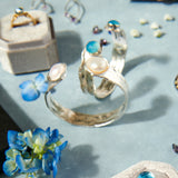 Collection of silver rings with gemstones on a light blue surface with flowers.