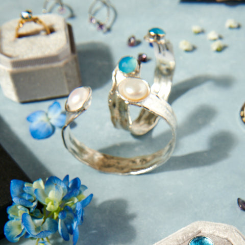 Collection of silver rings with gemstones on a light blue surface with flowers.
