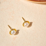 Gold earrings with pearl studs on a beige surface
