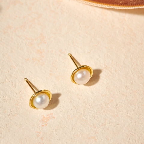 Gold earrings with pearl studs on a beige surface