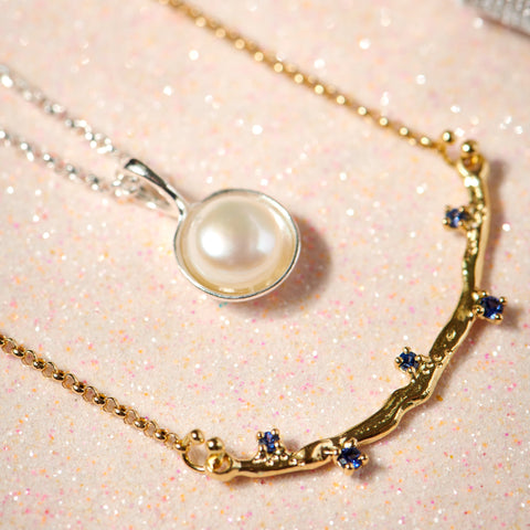 Gold necklace with a pearl pendant on a glittery pink background
