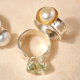 Silver ring with a pearl and green gemstone on a beige background