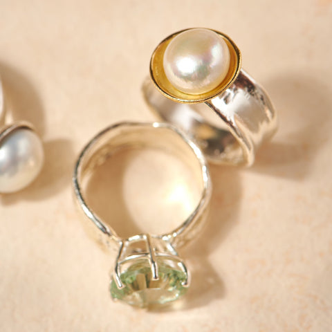 Silver ring with a pearl and green gemstone on a beige background